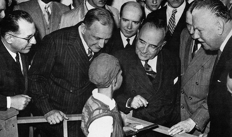  <strong> Getúlio Vargas conversa </strong> com aprendiz, durante visita à Feira Nacional da Indústria de 1942, tendo à sua direita o presidente da Fiesp, Roberto Simonsen, e à sua esquerda (de terno escuro) o interventor federal de São Paulo, Fernando Costa