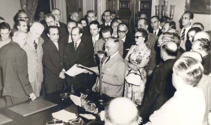  <strong> Getúlio discursa, </strong> observado por Café Filho (atrás dele) e pelo deputado Tancredo Neves (à direita de Café) durante solenidade de assinatura do decreto de criação da Petrobrás