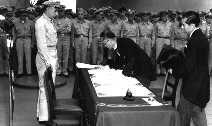  <strong> O premiê japonês Manoru Shigemitsu </strong> assina o termo de rendição, a bordo do “USS Missouri”, na baía de Tóquio, em 2 de setembro de 1945, observado pelo general Douglas MacArthur. Ao fundo, oficiais britânicos e norte-americanos assistem à cerimônia      