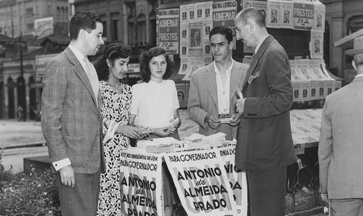       <strong> Em banquinha no centro de São Paulo, cabos eleitorais distribuem </strong> panfletos da campanha do candidato a governador de São Paulo Antônio de Almeida Prado (UDN), durante as eleições de 1947 